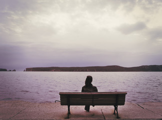Young woman on wooden bench  at seafront, soft focus nostalgic photo effect applied.