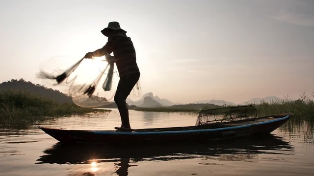 Slow Motion Silhouette of fishermen throwing fishing net during sunset with boats at the lake. Concept Fisherman's life style. Lopburi, Thailand.
