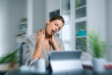 Dizzy young woman suffering neck cervical pain while working on her laptop at home.
