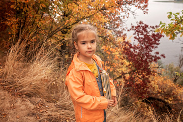 Smart cute kid girl holding a book with dry yellow leaves