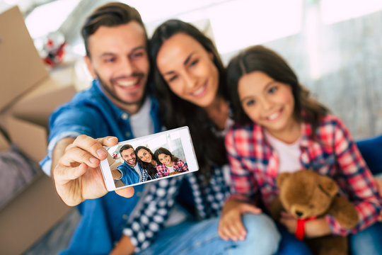 A photo for grandma. Delighted young couple and their kid are taking a joint selfie after moving to the new house.