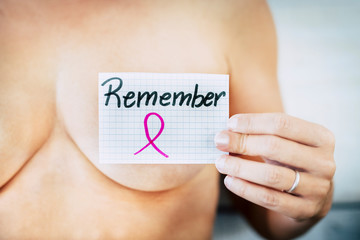 close up of nude caucasian woman holding a card of paper with written in the word remeber - concept of tumor and cancer prevention for women's day - healthy women fighting
