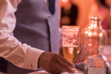 close up of hand of waiter serving a bottle with a glass of champagne or wine at the table - party or wedding