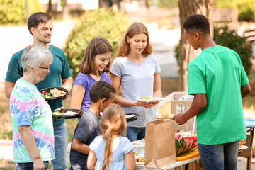 African-American volunteer giving food for poor people outdoors
