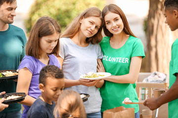 Young volunteers giving food to poor people outdoors