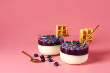 Glasses with blueberry dessert on color background