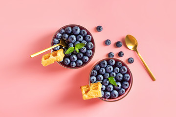 Glasses with blueberry dessert on color background