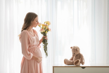 Beautiful pregnant woman with flowers near window