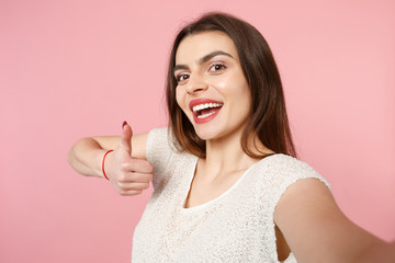 Close up of young woman in casual light clothes posing isolated on pink background, studio portrait. People lifestyle concept. Mock up copy space. Doing selfie shot on mobile phone, showing thumb up.