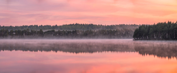 Wunderschöne Sonnenaufgangslandschaft mit nebliger Stimmung und ruhigem See am nebligen Sommermorgen in Finnland © VisitorImages