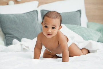 Cute African-American baby with soft towel on bed at home