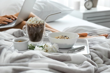 Young woman using laptop while having breakfast in bed