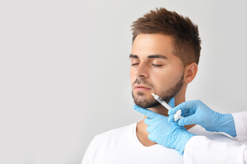 Handsome man receiving filler injection on grey background