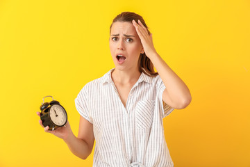 Worried young woman with alarm clock on color background