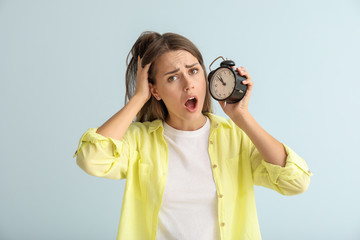 Worried young woman with alarm clock on color background