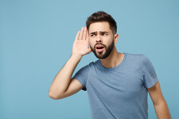 Young curious man in casual clothes posing isolated on blue wall background, studio portrait. People sincere emotions lifestyle concept. Mock up copy space. Try to hear you with hand near ear.