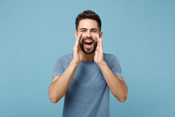Young handsome man in casual clothes posing isolated on blue wall background, studio portrait. People sincere emotions lifestyle concept. Mock up copy space. Screaming with hand gesture near mouth.