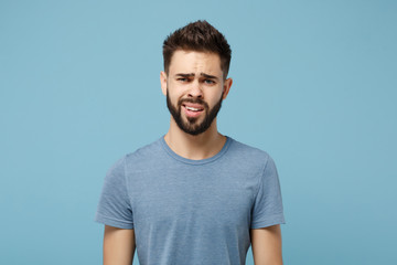 Young perplexed disgusted irritated man in casual clothes posing isolated on blue wall background,...