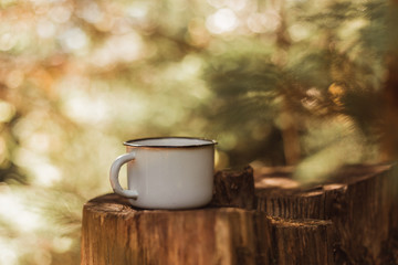 Mock up of coffee cup at green blur nature forest. Leisure lifestyle. Enameled cup of coffee or tea on wooden board in summer forest outdoors. Retro filter