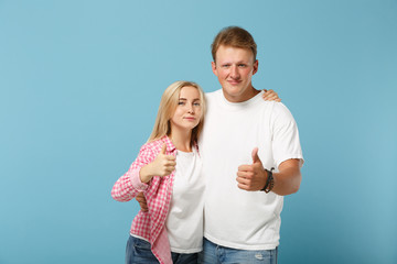 Young couple two friends guy girl in white pink empty blank design t-shirts posing isolated on pastel blue background studio portrait. People lifestyle concept. Mock up copy space. Showing thumbs up.