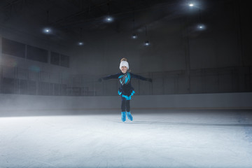 Fototapeta na wymiar view of child figure skater on dark ice arena background