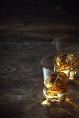 close up view of  two glasses with ice and whiskey on wooden background
