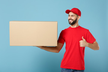 Delivery man in red uniform isolated on blue background, studio portrait. Male employee in cap...