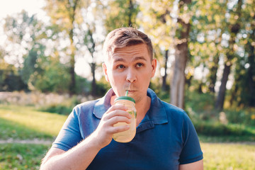 Fototapeta premium Young crazy man drinking a mojito and thinks something. A man outdoors, immersed in nature, drinks a glass of homemade lemonade. Vitamins and regular life concept