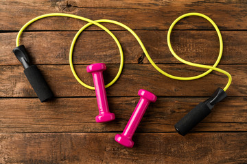 Dumbbells and jumping rope on retro wooden floor. Sport background