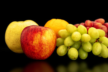 Orange, grapes, apple and pyrus pyriflora on a black background.