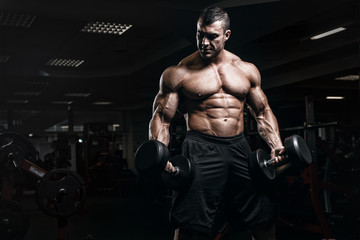 Fototapeta na wymiar Muscular athletic bodybuilder fitness model training arms with dumbbells in gym. Concept sport photo of exercises in gym
