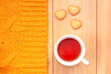 Cup of tea, cookies and knitted plaid on wooden background. Cold weekend at cozy home. Fall season. Cute autumn still life. Autumnal mood concept.