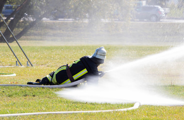 male lifeguard fireman holds a fire hose with a stream of water on the grass