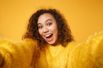 Close up of excited young african american girl in fur sweater posing isolated on yellow orange...
