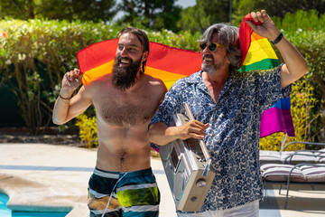 Portrait of a gay couple walking by the pool with a rainbow flag.