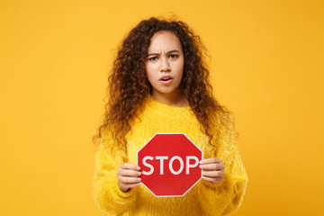Concerned young african american girl in fur sweater posing isolated on yellow orange wall...
