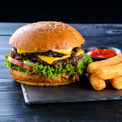 Burgers with juicy cutlet, fresh vegetables, crispy bun with sesame seeds on a wooden table. Traditional fast food.