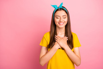 Portrait of cute hipster closing her eyes touching chest wearing yellow t-shirt isolated over pink background - obrazy, fototapety, plakaty
