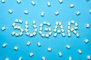 The inscription SUGAR made by lump sugar on a colored background. Minimal creative concept