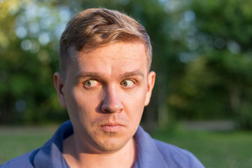 Portrait of a young guy on nature background. Puzzled confused bewildered shocked amazed man....