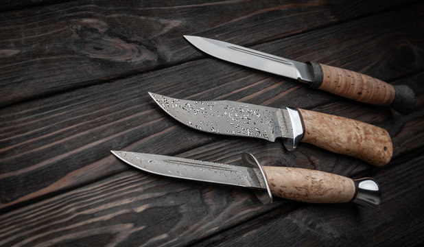 Hunting bowie knife with a wooden handle on dark wooden background. Steel arms weapon. top view