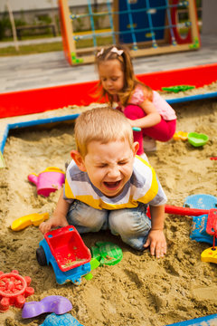 Crying unhappy boy play with car in sandbox