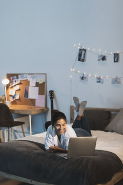 Long shot smiling woman working on laptop in bed