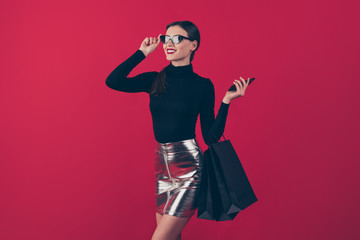 Portrait of her she nice-looking attractive pretty gorgeous cheerful dreamy lady holding in hand cell carrying black bags new things isolated over maroon burgundy marsala red pastel color background