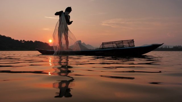 Silhouette of Fishermen pull fishing net rising out of the water After throwing fishing net away During sunset with boats at the lake. Concept Fisherman's life style. Lopburi, Thailand. Slow Motion