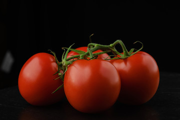 whole red tomatoes with green stems. on dark background. close up