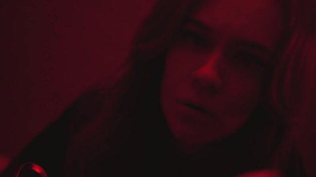 Young girl catches visual hallucinations in front of a mirror of a dark red room