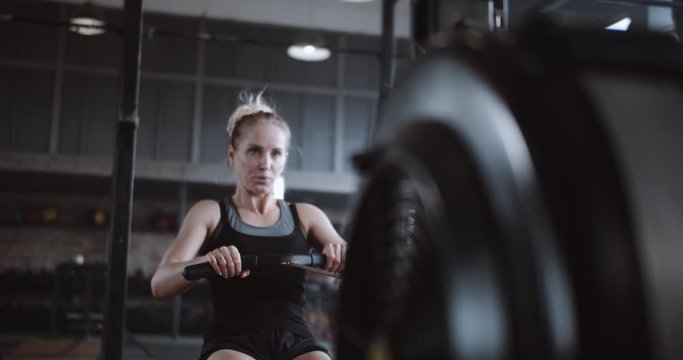 Beautiful young successful blonde woman working out on stationary rowing machine in gym. Healthy lifestyle slow motion.
