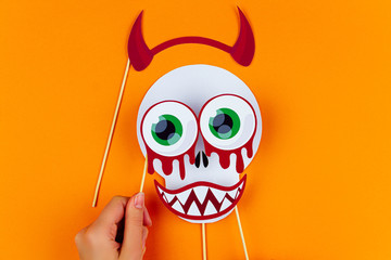 Funny face of skull monster with red horns, blood eyes and vampire smile on orange background....