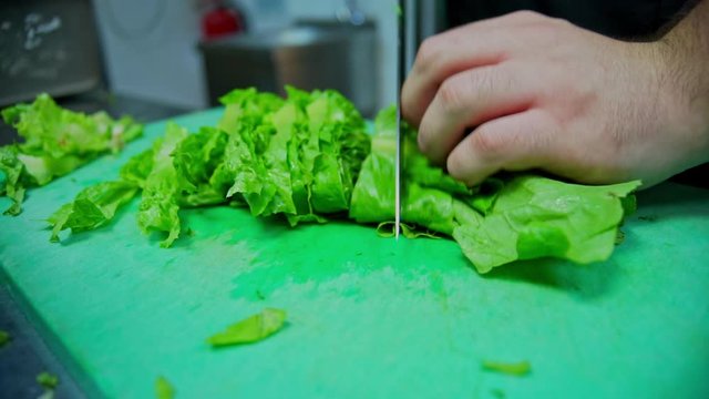 Close up footage of cook cutting lettuce on green teflon board